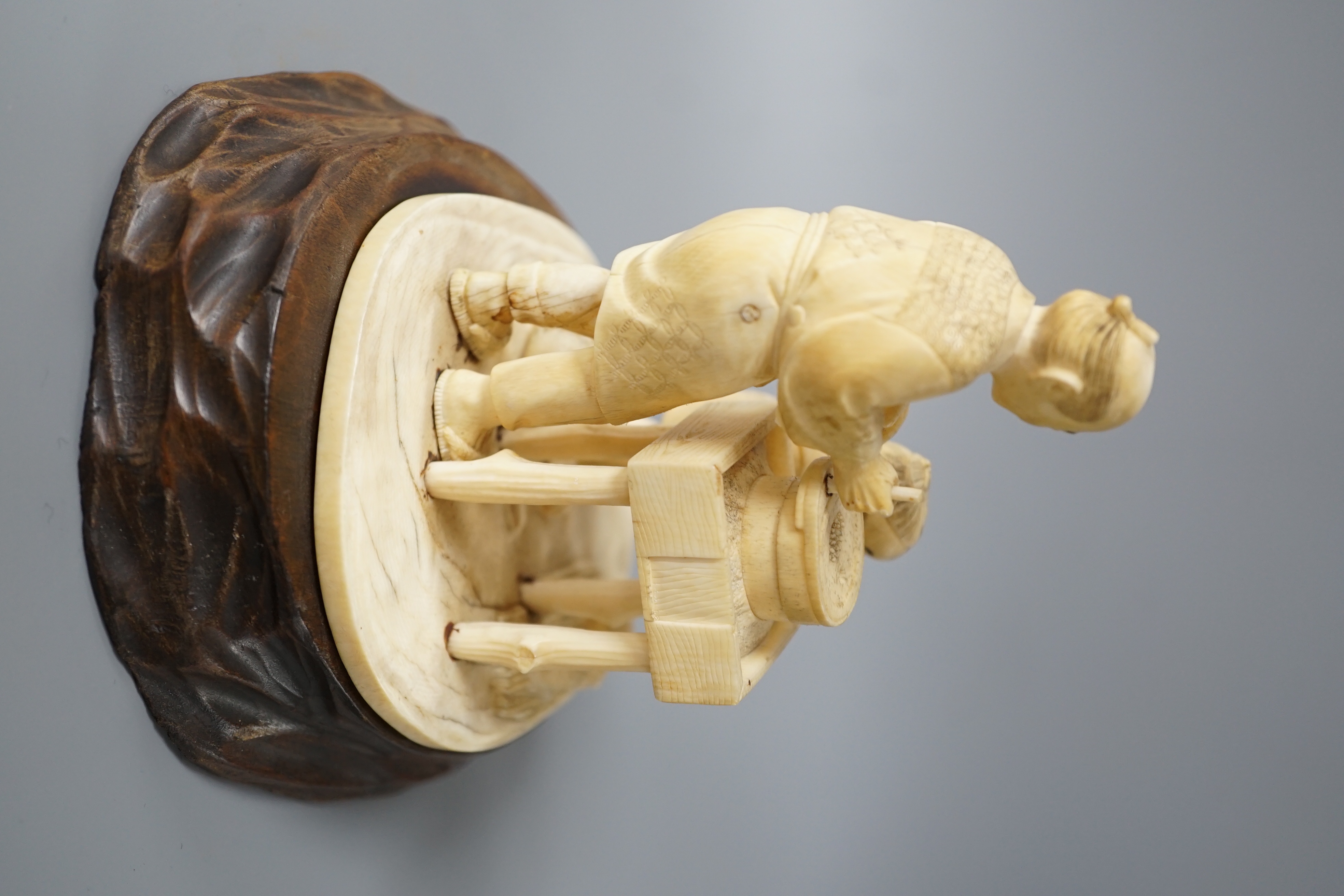 A Japanese ivory okimono of man and boy at a grindstone, Meiji period, signed, wood stand. 15cm total height